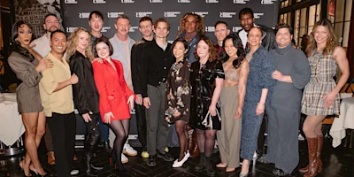 A group of people pose together in front of a backdrop at an indoor event, all dressed in a variety of stylish outfits.