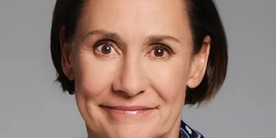 A middle-aged woman with short brown hair smiles softly at the camera against a plain background.