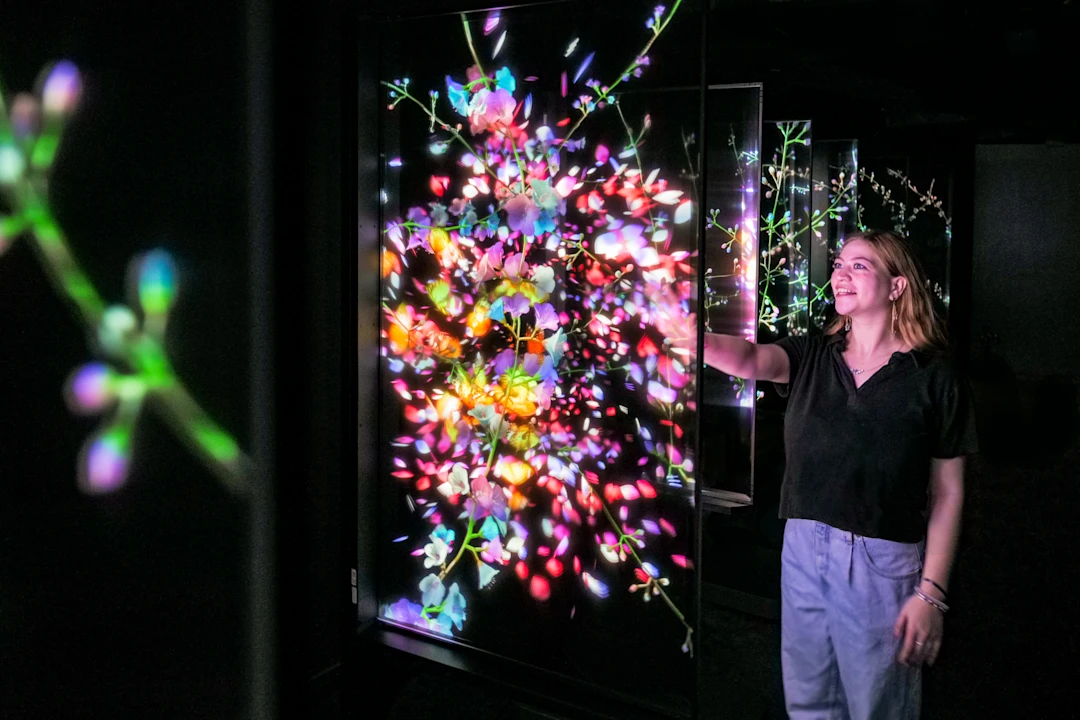 Production photo of Blooming Wonders in Washington showing, a woman interacts with a vibrant digital art display featuring colorful floral patterns on a dark background.