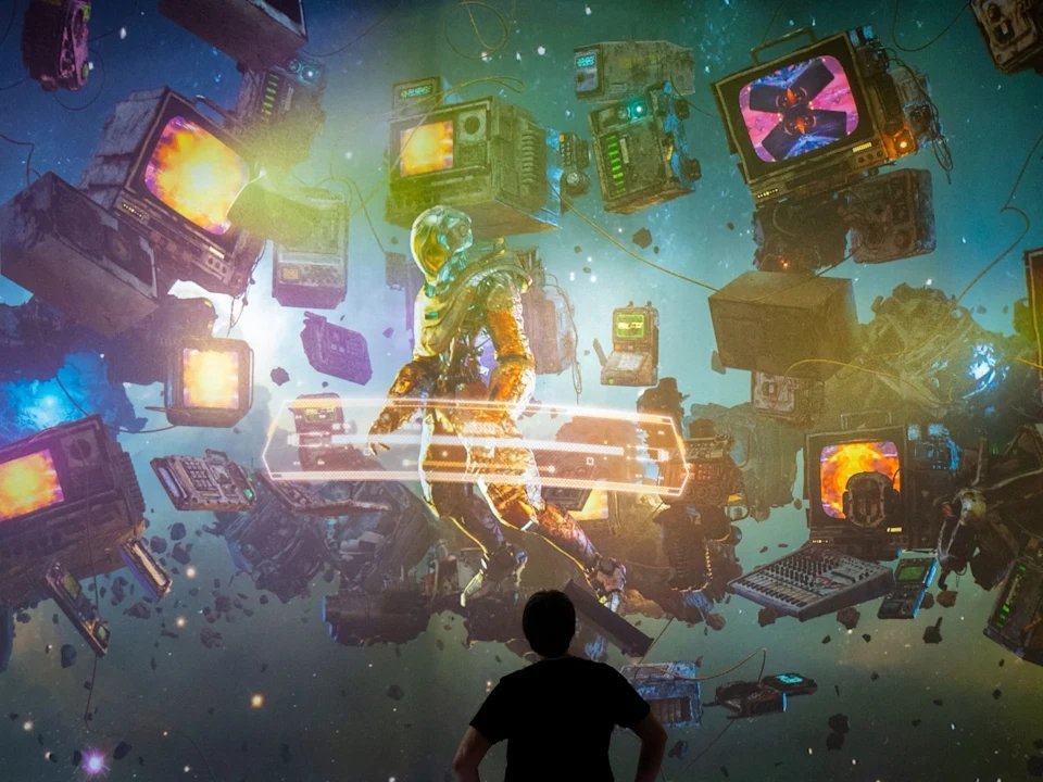 A person stands facing a large, colorful mural of an astronaut surrounded by floating retro computers and electronics in a cosmic setting.