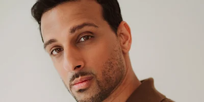 A man with short dark hair, trimmed beard, and neutral expression looks at the camera against a plain background.