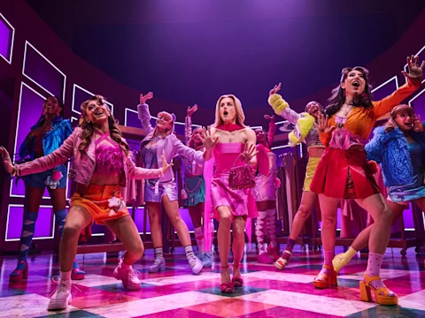 The ensemble sings and dances with jazz hands in a bright pink boutique dressing-room set.