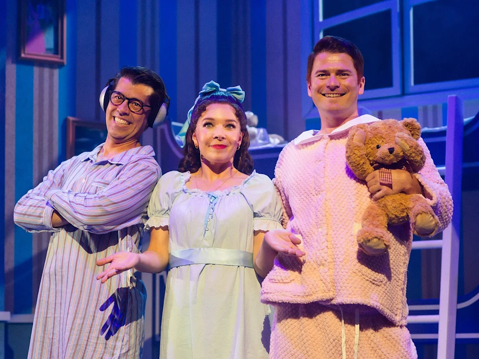 Three actors in pajamas stand on a stage, with the man on the right holding a teddy bear.