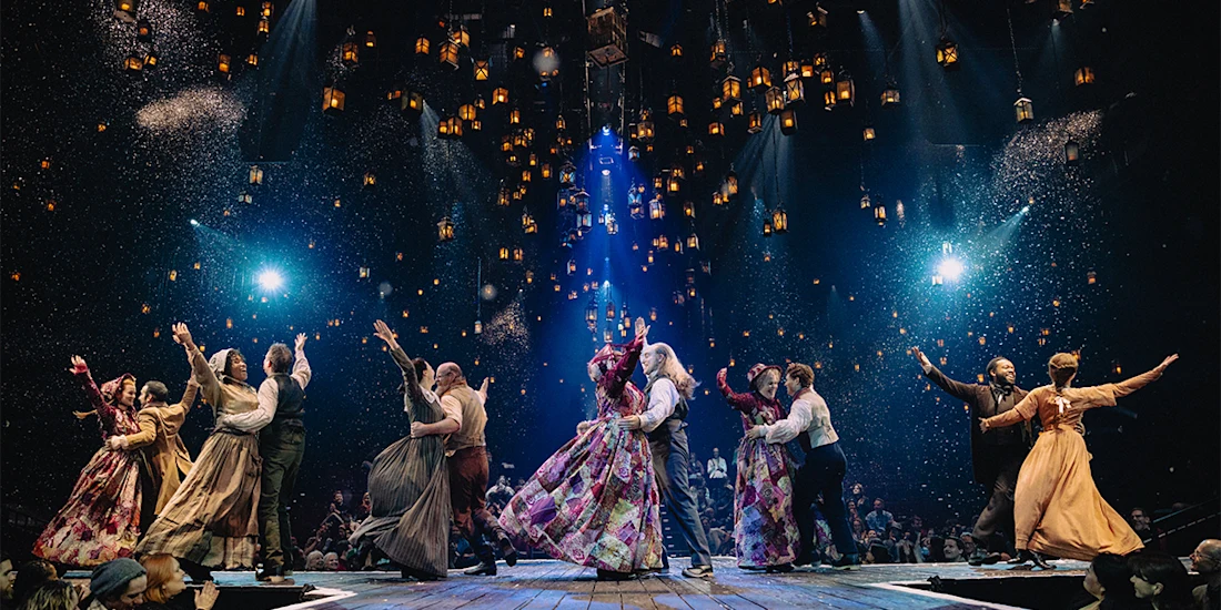 Actors in period costumes dance in pairs on a stage, surrounded by floating lanterns and illuminated by spotlights, with an audience seated around them.