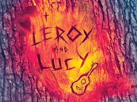 A tree bark has the names "Leroy and Lucy" and a small guitar drawing carved into it, with a background resembling flames.