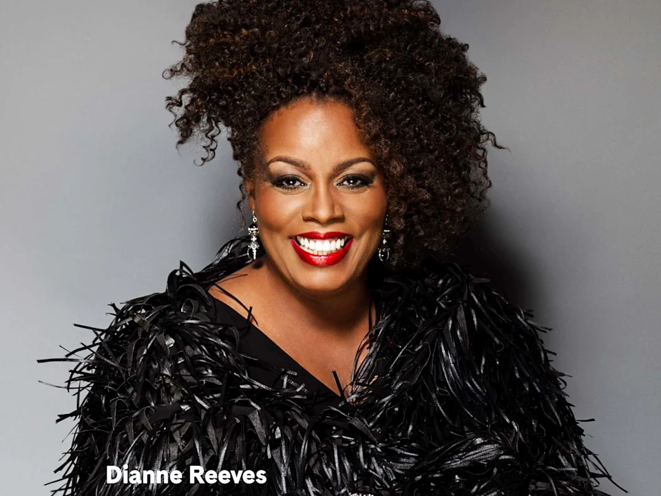 Portrait of jazz singer Dianne Reeves smiling against a gray background.