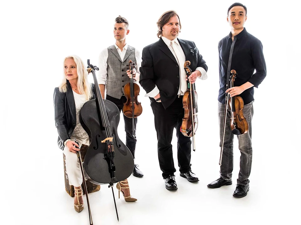 Four musicians pose with string instruments against a white background; three stand holding violins or violas, one sits holding a cello.