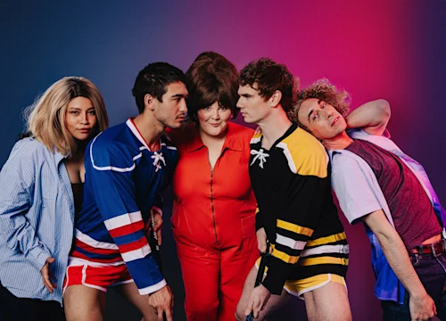 Five people pose together against a gradient pink and blue background, wearing colorful retro sports outfits and casual clothing.
