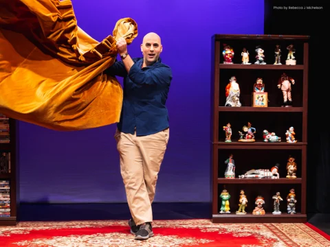 Production photo of Clowns Like Me in New York, featuring Scott Ehrenpreis in a blue shirt and beige pants pulling a yellow curtain.