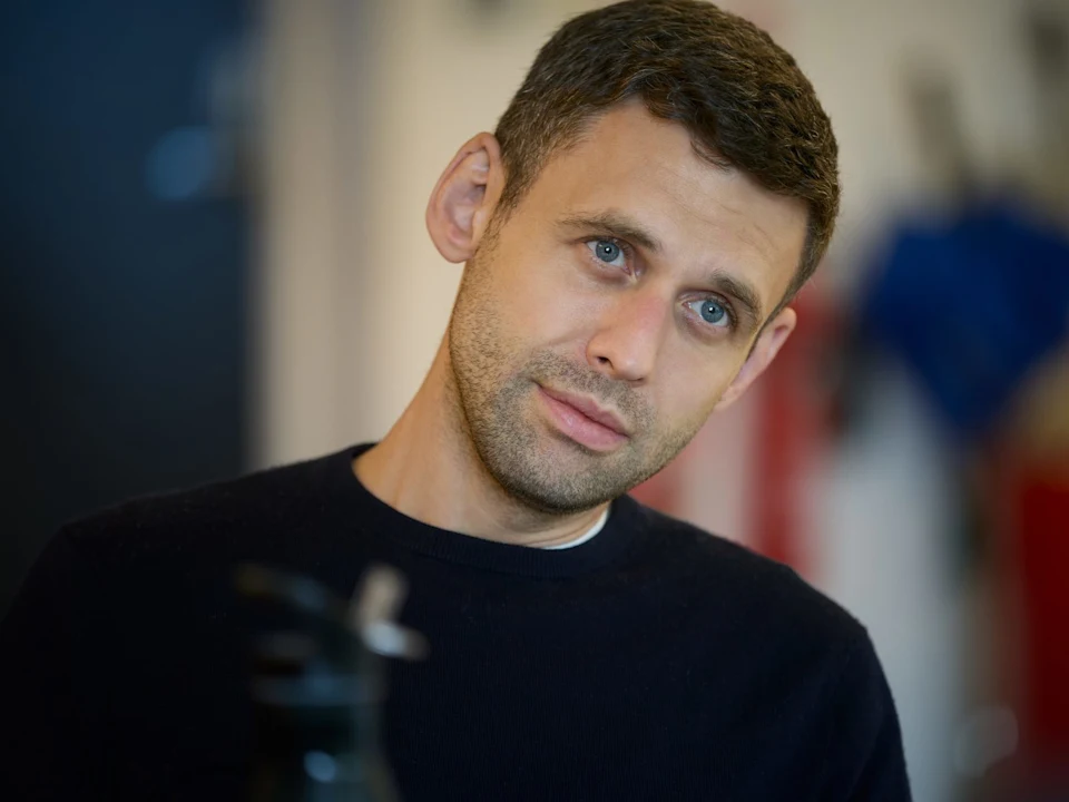 A man with short brown hair looks thoughtfully off-camera during a Holy Fool rehearsal.
