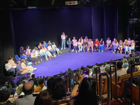 A group of people seated on stage in a theater, with an audience watching them.