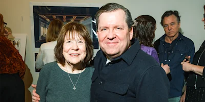 A group of people standing indoors at what appears to be an art exhibit or gallery, with two people in the foreground smiling at the camera.