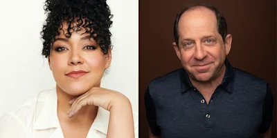 A woman with curly hair and a white shirt poses with her hand under her chin next to a man in a blue collared shirt, both facing the camera.