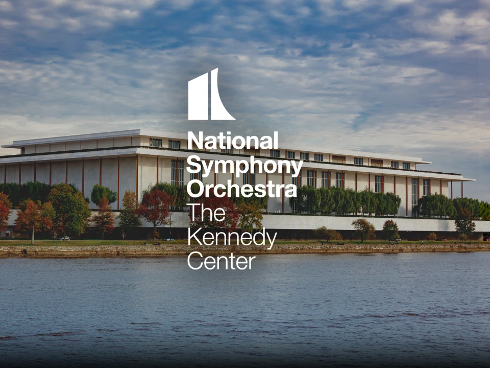 National Symphony Orchestra at The Kennedy Center, a large modern building by the water, with trees and a cloudy sky in the background.