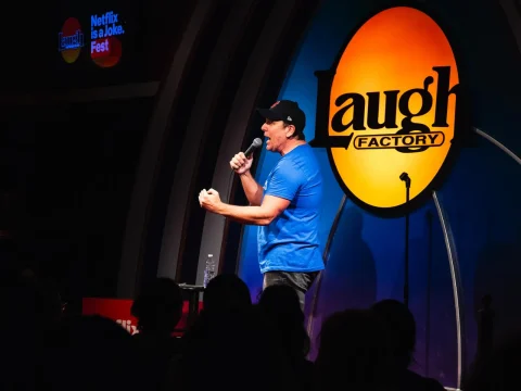 Comedian on stage at the Laugh Factory, performing in front of a live audience, with a microphone.