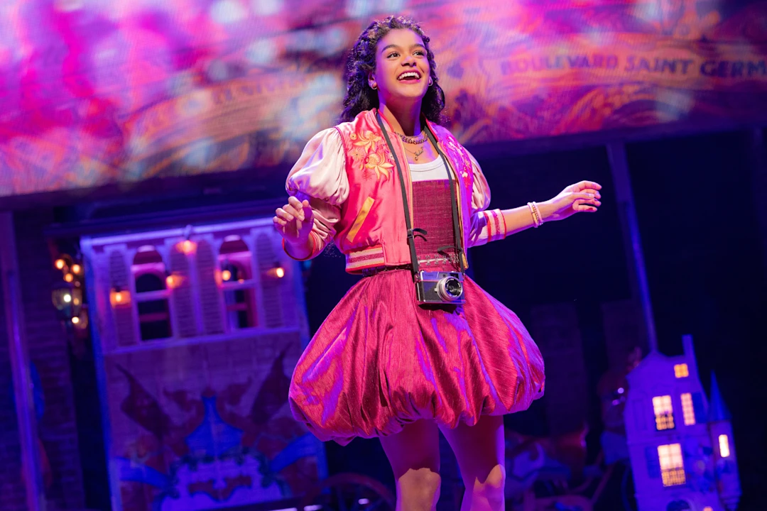 Production photo of & Juliet in New York, showing Gianna Harris with colorful set pieces and lights in the background.