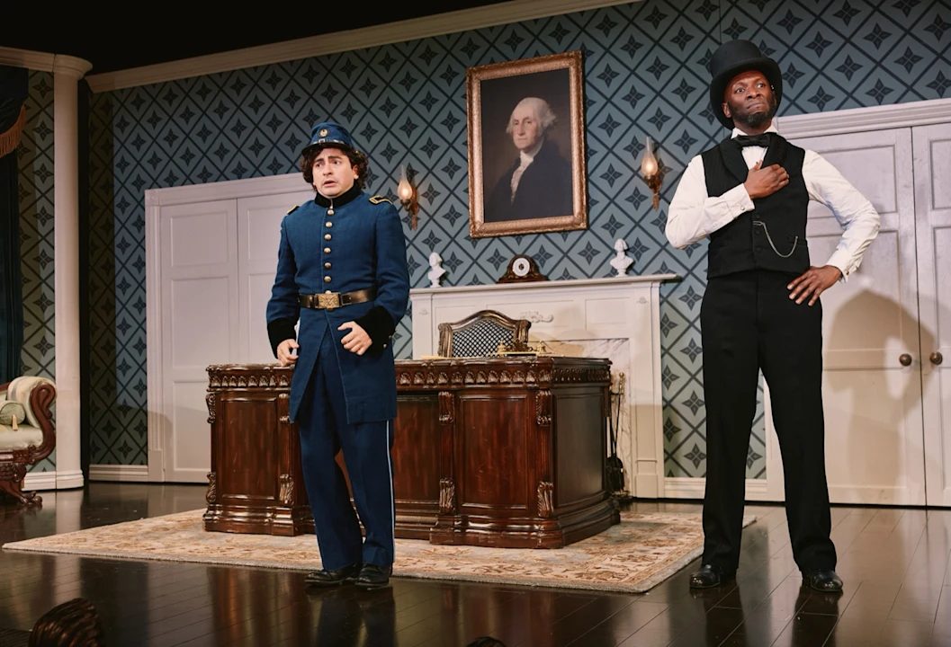 Two performers in a period drawing room, one in a blue Union army uniform, the other in a black waistcoat and top hat.
