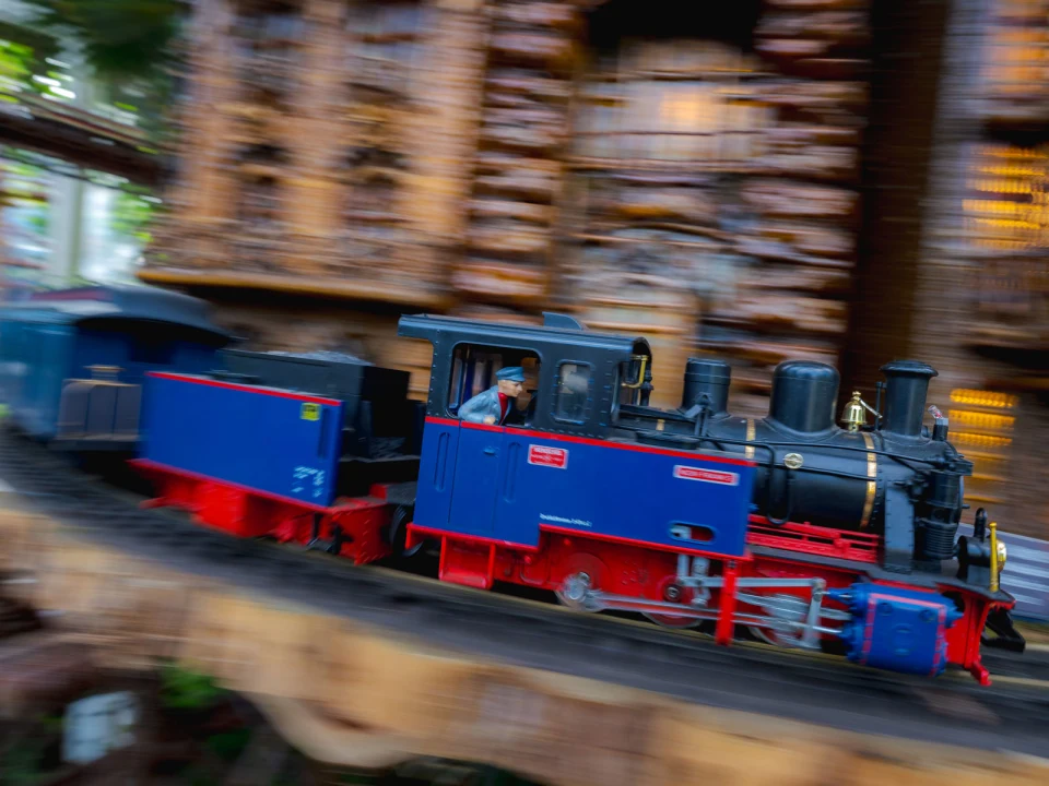 A blue and red toy train moves quickly on a track with a blurred background, suggesting motion.