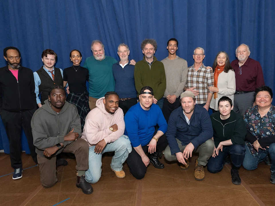 A group of 17 people pose together in front of a blue curtain, with some standing and others crouching or kneeling.