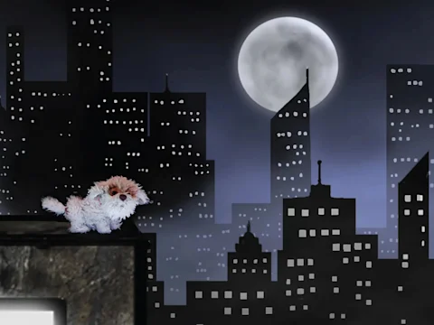 A small stuffed dog sits on a ledge in front of a dark city skyline at night, with a full moon in the sky.