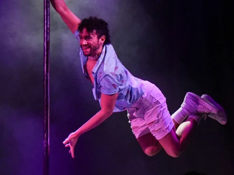 Production Photo of Schtick A Pole In It: a comedy & pole dancing show in New York, showing a man performs an acrobatic move on a pole.