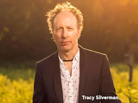 A portrait of violinist Tracy Silverman in a dark blazer, outdoors at sunset.