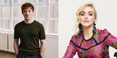 A man with short curly red hair in a dark shirt stands indoors; next to him, a woman with long blonde hair in a colorful patterned dress poses against a plain background.