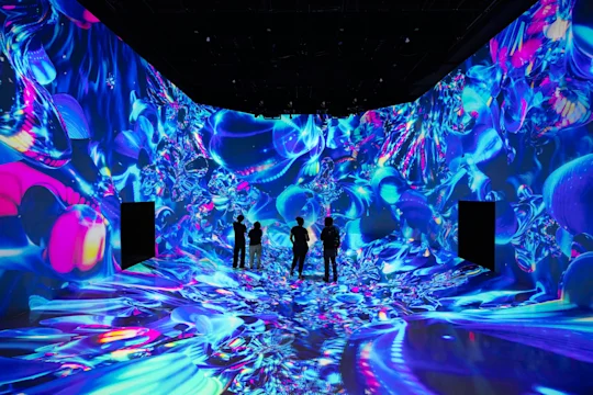 People stand in a room with vibrant blue and purple digital art projections covering the walls and floor.