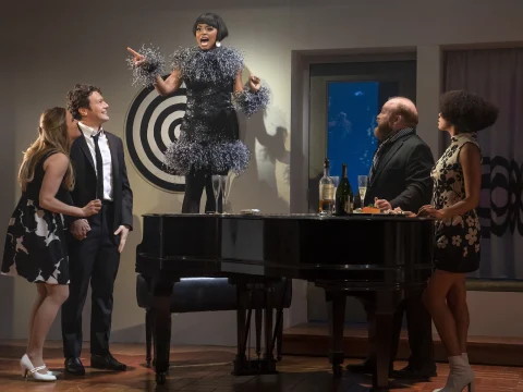 Production shot of Merrily We Roll Along in New York, with Krystal Joy Brown as Gussie Carnegie standing on a piano seat, with Katie Rose Clarke as Beth, Jonathan Groff Jonathan Groff as Franklin Shepard, Jacob Keith Watson and Talia Robinson.