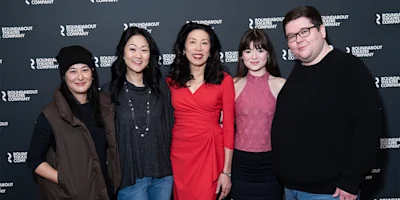 Five people standing and posing for a group photo in front of a Roundabout Theatre Company step-and-repeat backdrop.