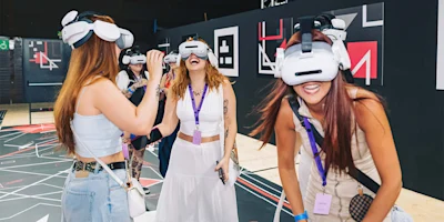 Four women wearing VR headsets stand together indoors, interacting and smiling, in a modern, tech-themed space with abstract wall designs.