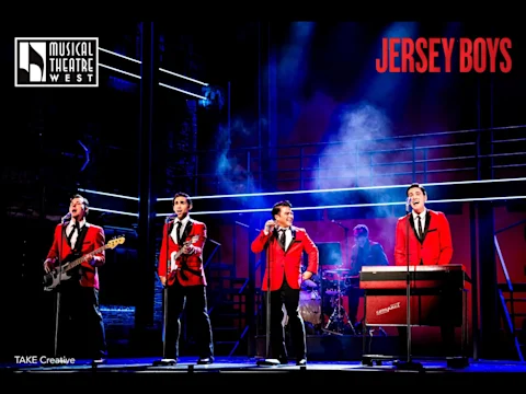 Four performers in red jackets sing and play instruments on stage under dramatic lighting, with "Jersey Boys" signage above.