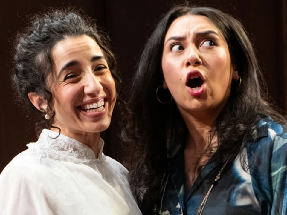 Two women side-by-side; one is laughing while the other has an expression of surprise with her mouth open.