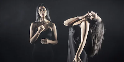 Two women in black dresses stand against a dark background; one faces forward with a neutral expression, while the other tilts her head back dramatically.