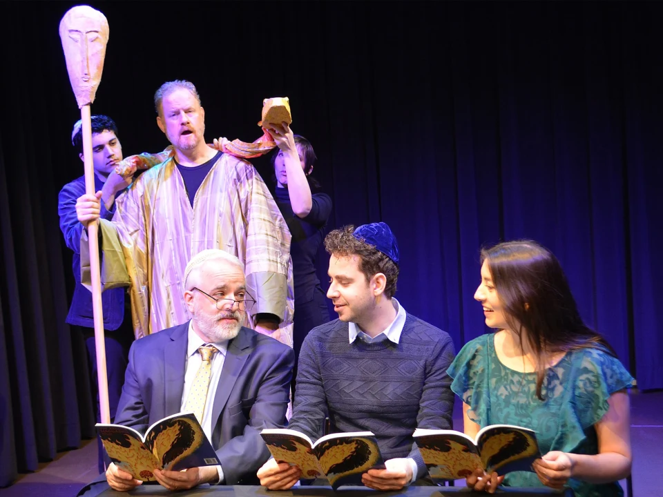 Production shot of Exagoge in New York, showing ensemble talking while holding books.