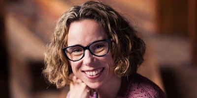 A smiling woman with curly hair and glasses.