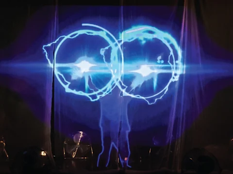 Performer on stage with blue circular light projections, creating an ethereal effect.