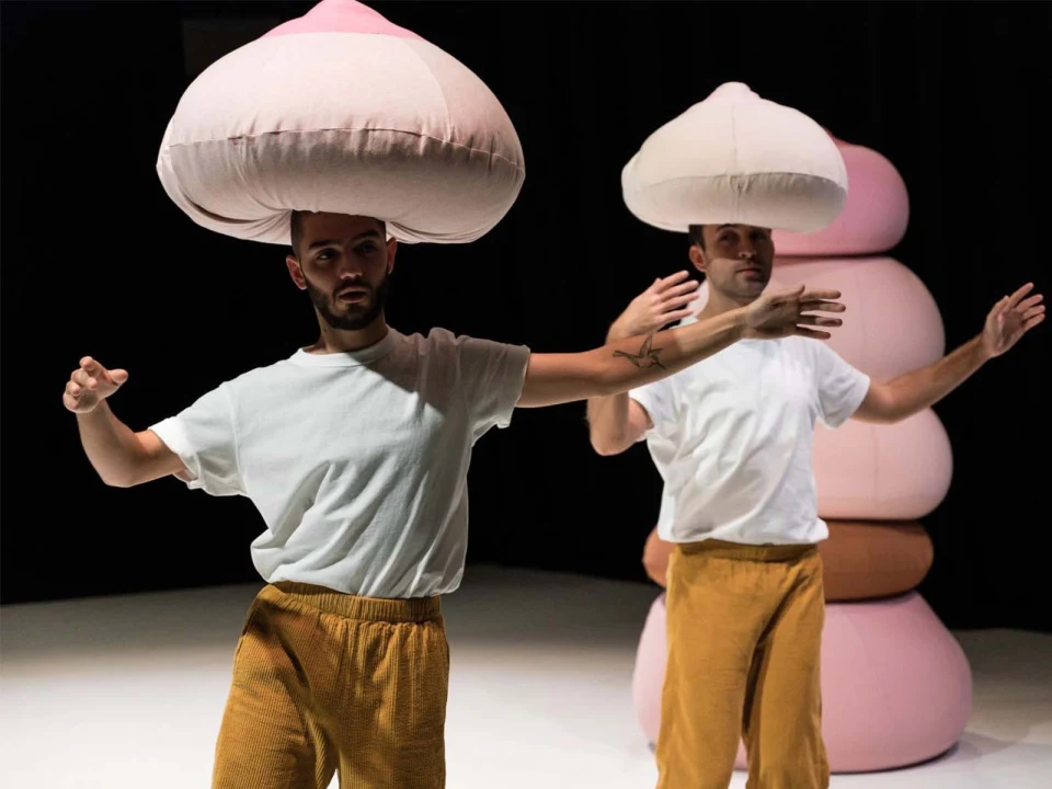 Two people wearing large, rounded hats and yellow pants perform a dance.