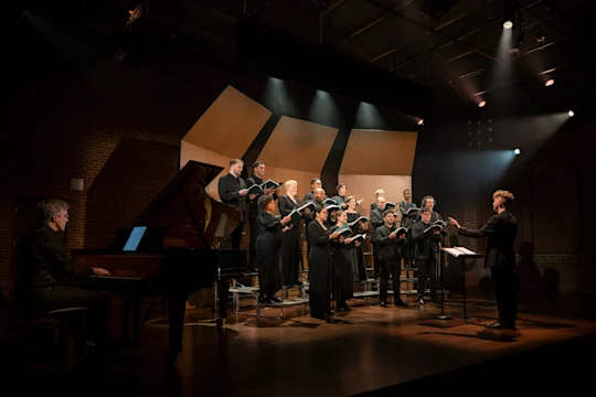 A choir performs on stage with a piano and a conductor.