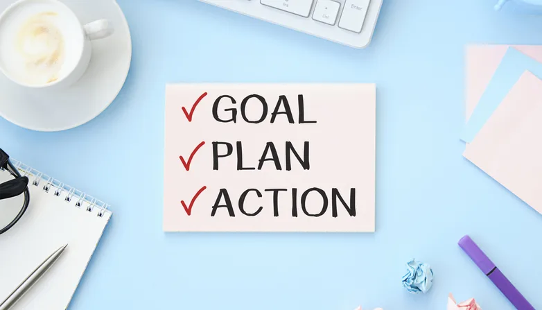 Goal, plan, action text on notepad with office accessories on a wooden background.