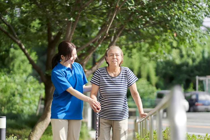 A caregiver helps an older woman walking with a cane.