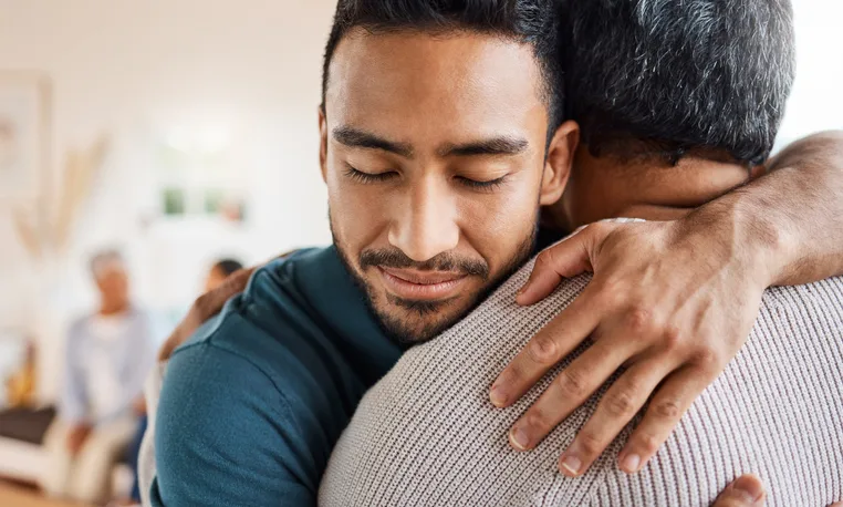 A young man is hugging an older man, showing emotional support.