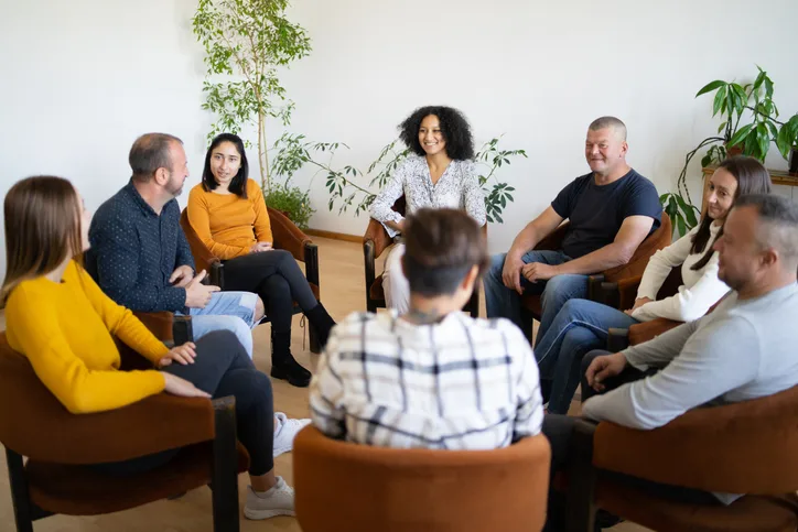 People sitting in chairs in a circle, talking to one another.