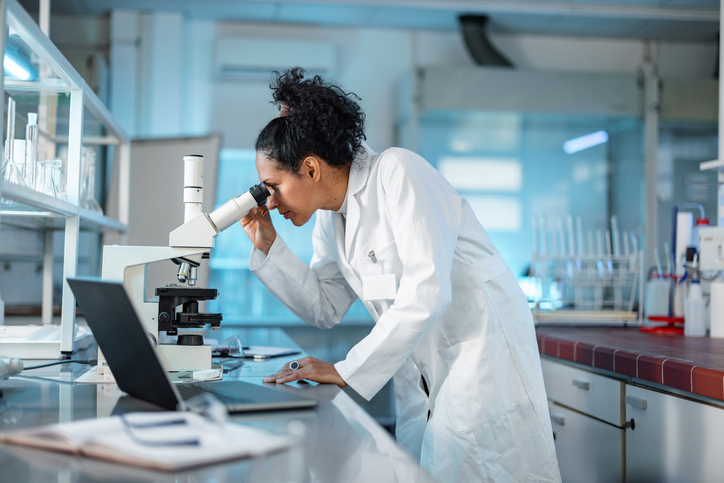 Laboratory research being conducted by a female scientist looking through a microscope.