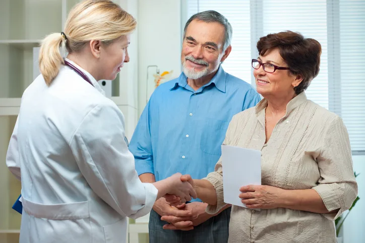 An older couple speaks with their doctor in a medical setting.
