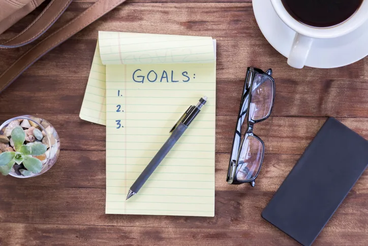 Notepad titled "Goals" with a pen and pair of glasses on the table.
