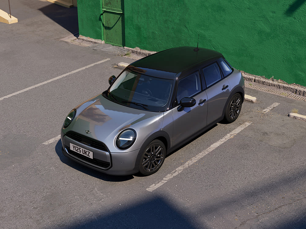 Aerial view of a gray MINI Cooper 5 door parked in a parking lot with a green wall at the back