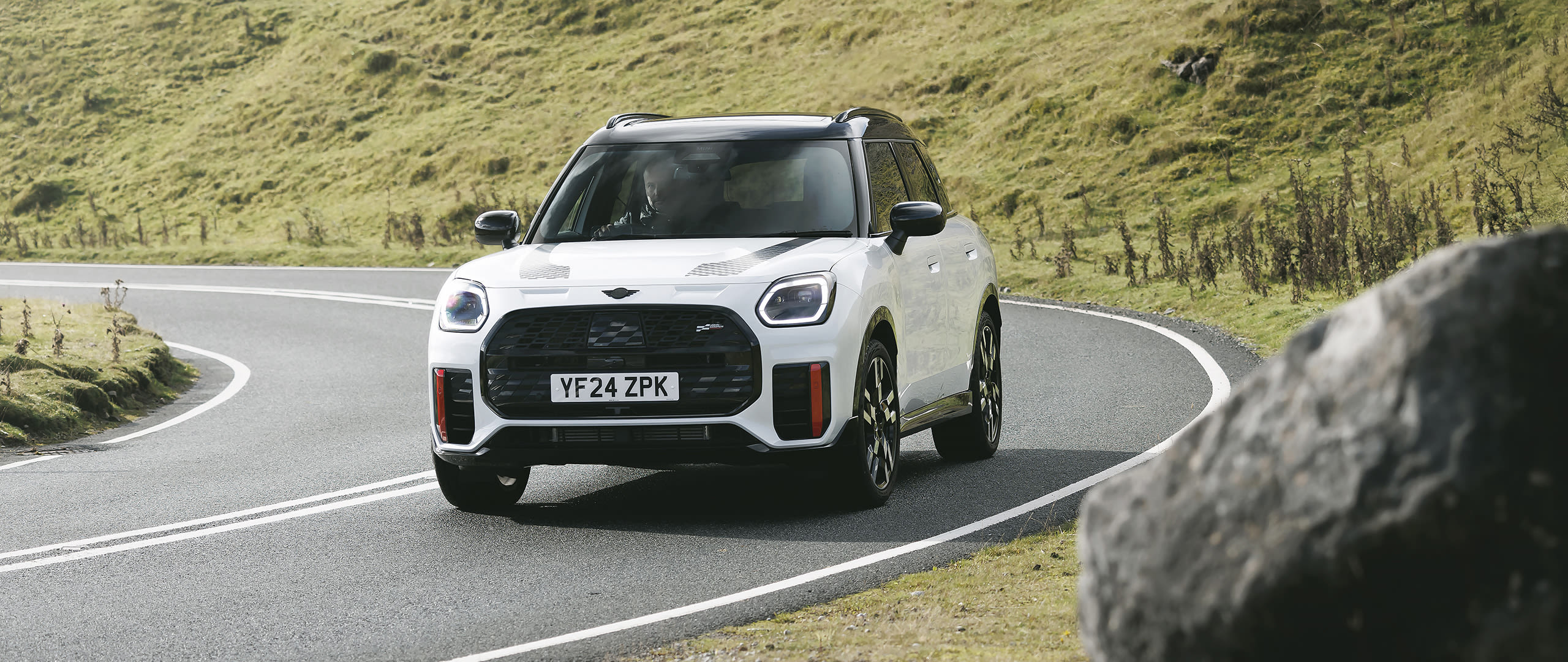 White MINI Countryman facing forward on a public road between hills.