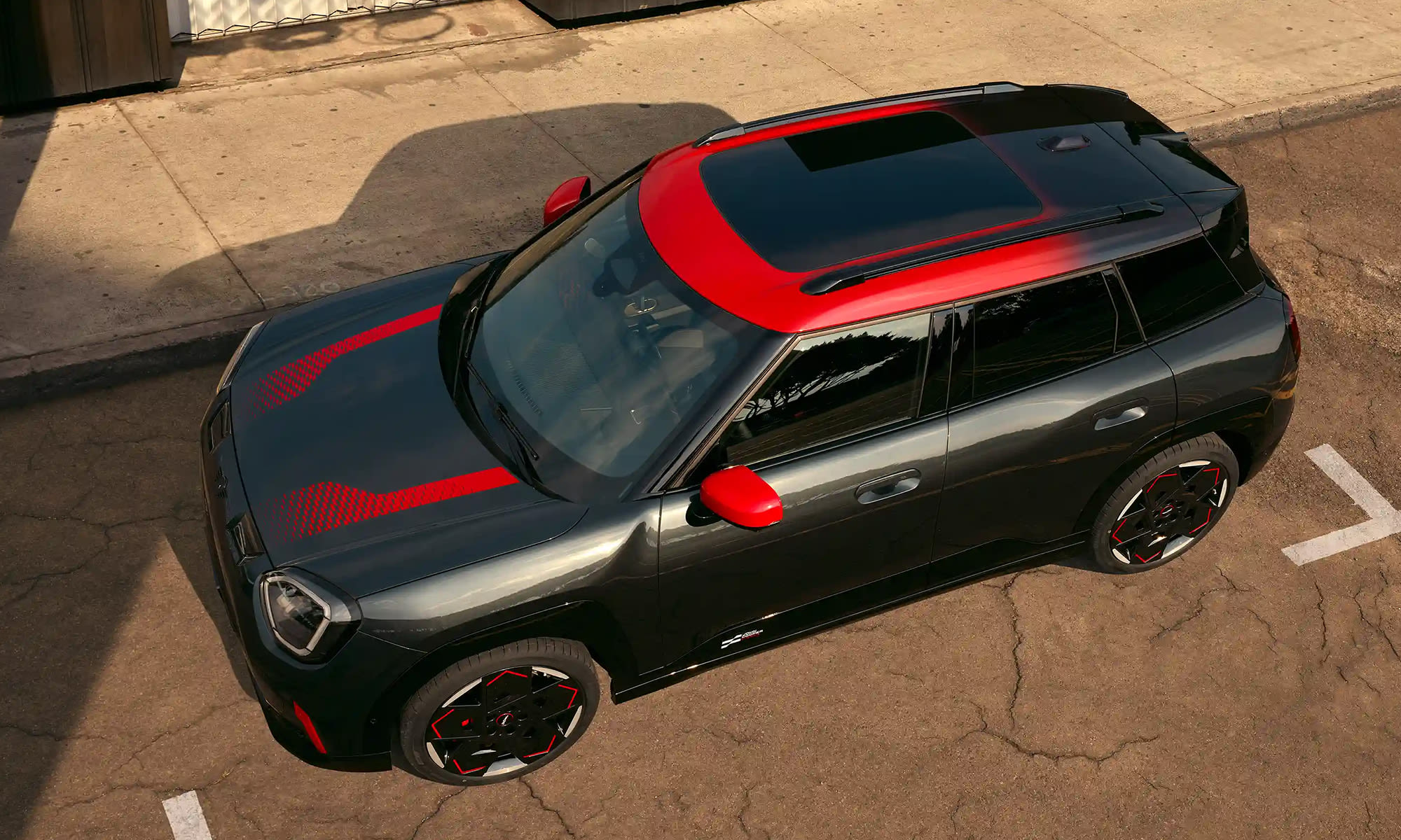 Top‑down view of a MINI John Cooper Works with a red two‑tone roof parked on a city street.