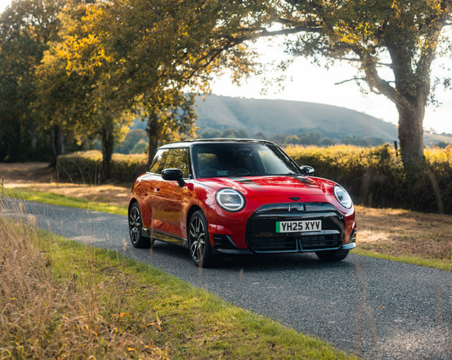 Red JCW MINI Cooper Electric on a country road with trees on left sides of the road.